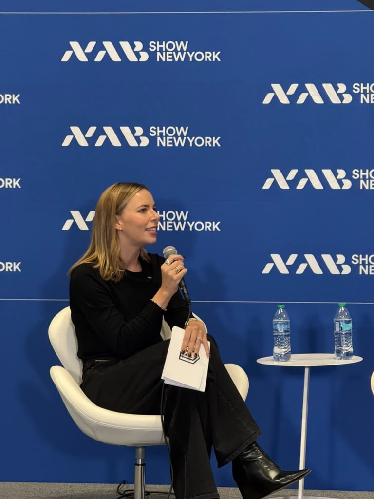 Anne Singer on the NAB Show New York stage, holding a microphone and her notes